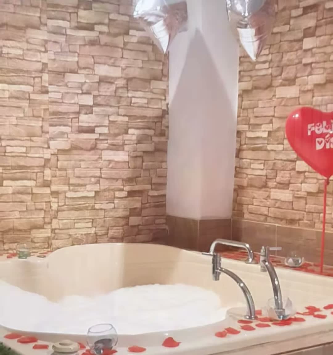 Jacuzzi con espuma, pétalos de rosa y muro de piedra